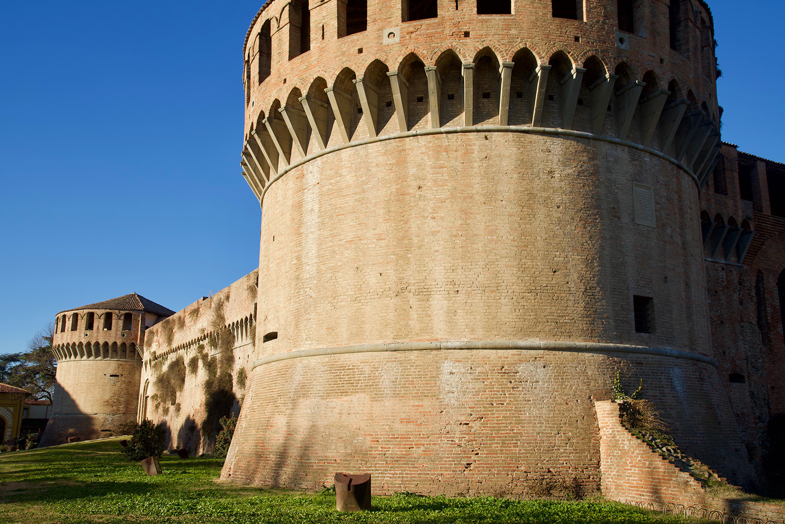 Rocca di Imola. si vede un robusto torrione circolare in primo piano, con scorcio su mura e un secondo torrione sullo sfondo.